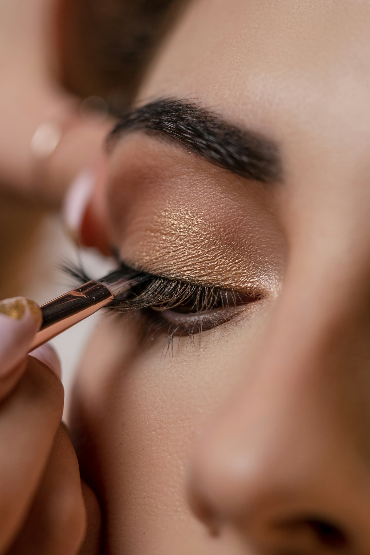 A makeup artist applying gold eyeshadow to a client's eyelid with a fine brush