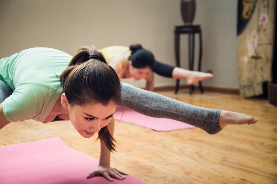 Two clients holding a balance pose on pink mats in a warm-lit pilates studio